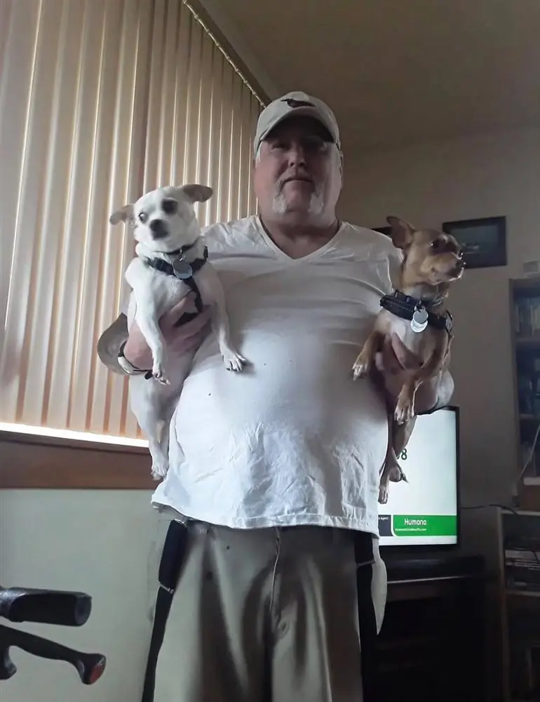 Man holding two Chihuahuas, one white and one fawn, in his living room